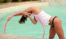 Brillentragende Teenager-Freundin mit Zöpfen posiert mit einem Hula-Hoop im Pool